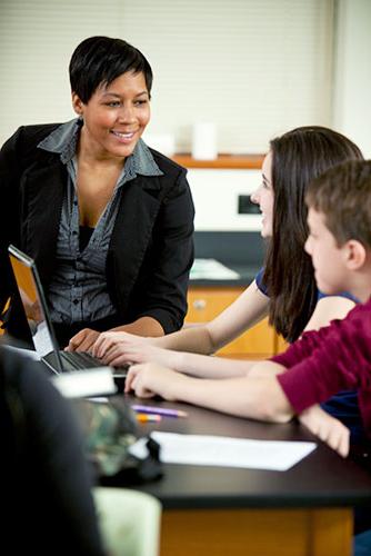 Female teacher speaking to high school aged children at a desk